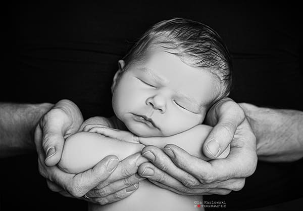 Ein schlafendes Baby in Frontalansicht. Babyfotografie professionell: Ein schlafendes Baby in Frontalansicht. Das Köpfchen liegt auf seinen verschränkten Ärmchen. Diese wiederum liegen in Papas Händen.