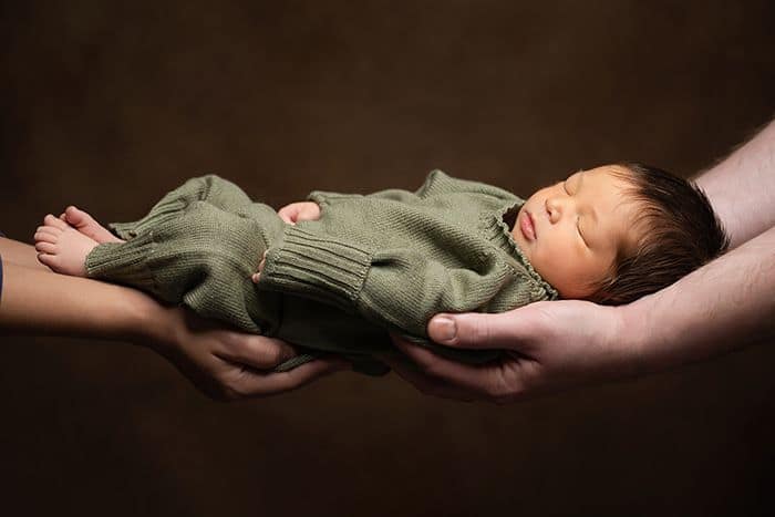 Ein Baby, das auf den Händen seiner Eltern getragen wird. Es schläft dabei. babyfoto mit Eltern. kleines schlafendes Baby auf einer Babyfotografie. das baby schläft auf den Händen seiner Eltern. Das Babyfoto ist im Querformat. Die Hände der Eltern greifen von links und rechts in das Bild hinein und halten das Baby fest. babyfotografie duesseldorf
